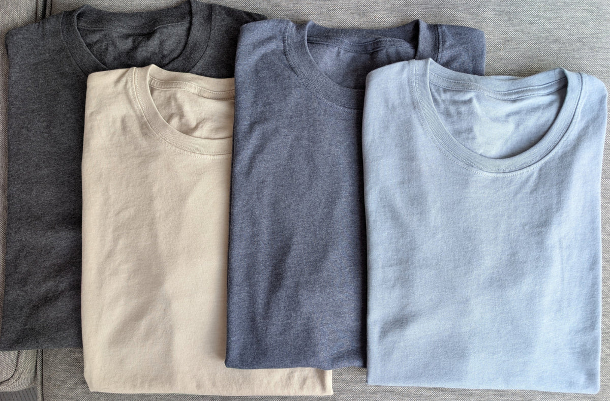 Four folded Nautically Nice Coastal Tees in Nightnoir, Dunedrift, Moormist, and Skystone displayed side by side on a grey surface