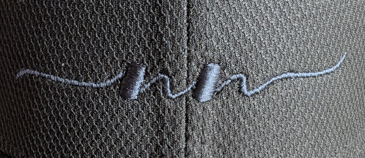 Close-up of the embroidered Nautically Nice double wave logo across the front panel seam of the Coastal Cap