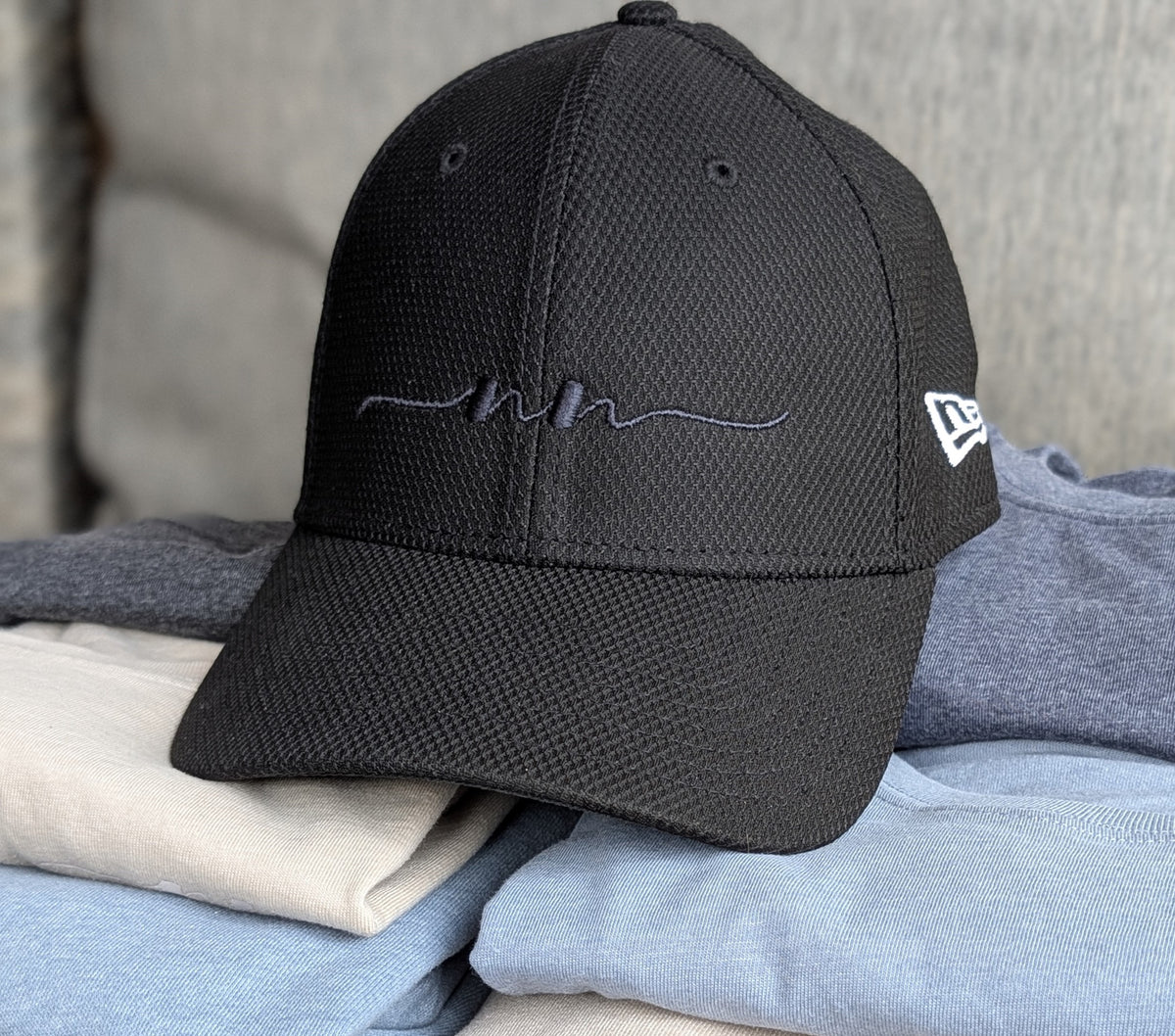 Nautically Nice Coastal Cap in black resting on folded Coastal Tees in Dunedrift, Skystone, and Nightnoir with New Era branding visible