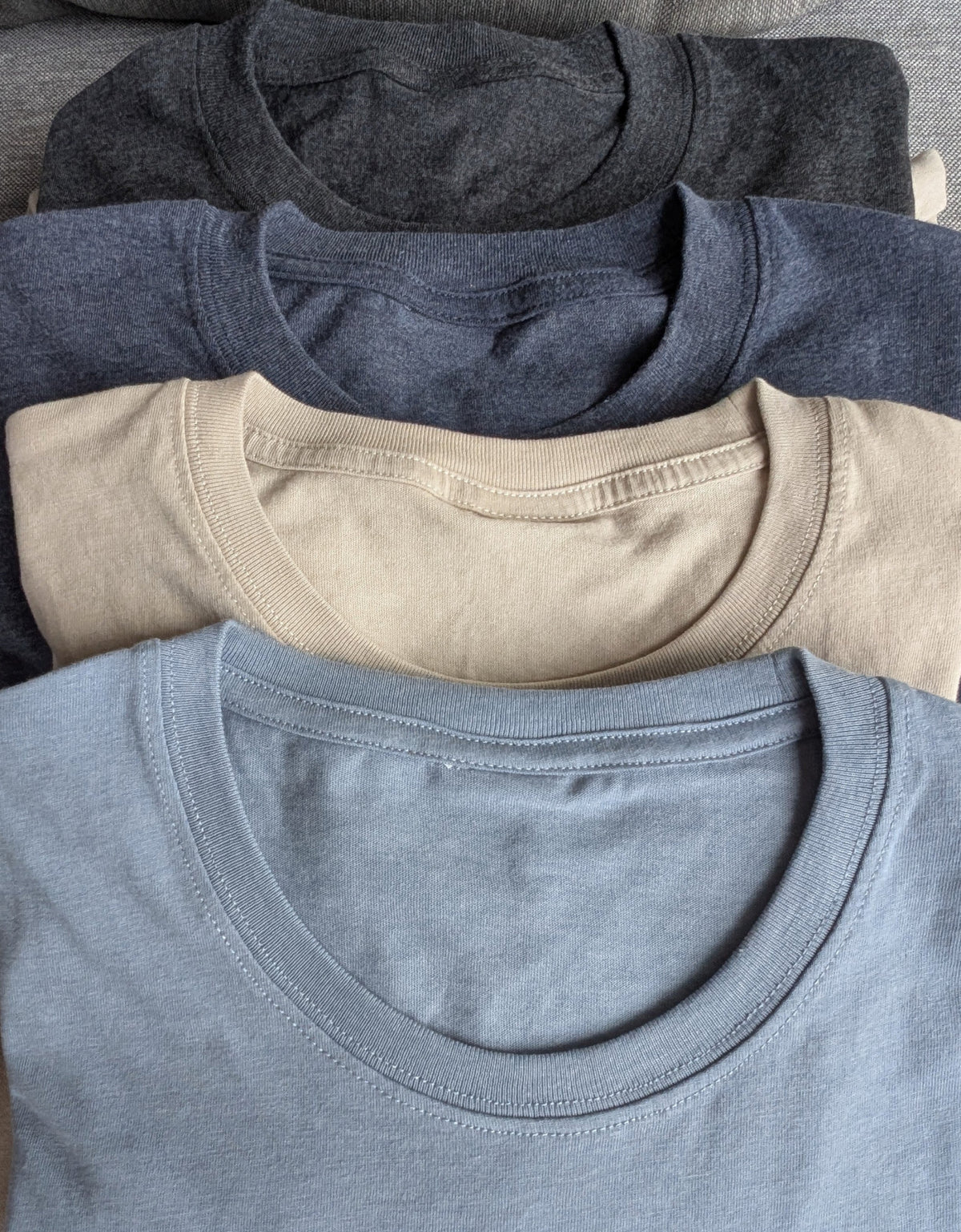 Close-up of four stacked Nautically Nice Coastal Tees in Skystone, Dunedrift, Moormist and Nightnoir showing fabric texture and ribbed neckline detail